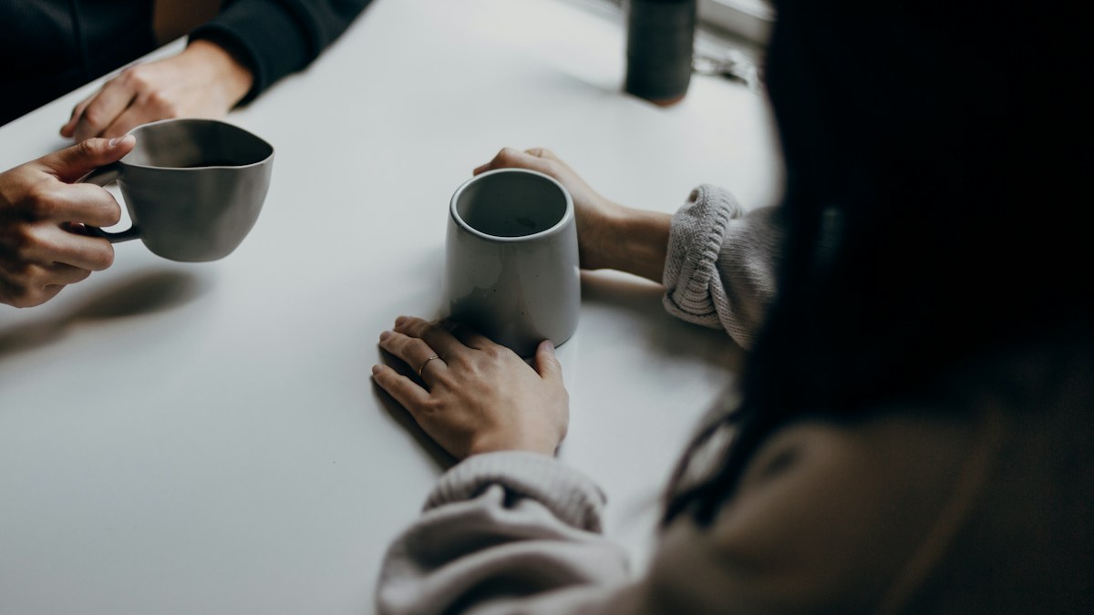 テーブルでマグカップを持ちながら向き合う二人の手元